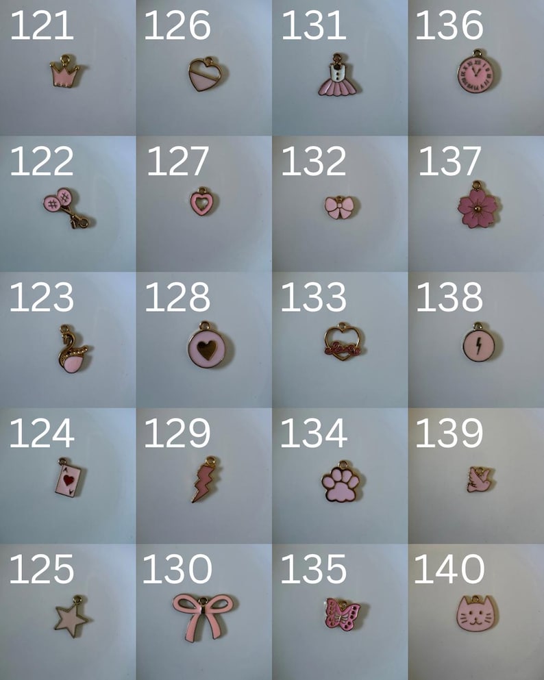 K&ouml;nnte beinhalten: Eine Sammlung von zwanzig kleinen Metallanh&auml;ngern mit rosa Emaille-Details, die jeweils mit einer Nummer von 121 bis 140 beschriftet sind. Die Anh&auml;nger haben verschiedene Formen, darunter eine Krone, Herzen, ein Kleid, eine Uhr, ein Schwan, eine Spielkarte, ein Stern, eine Schleife, eine Pfote, ein Schmetterling, ein Blitz, eine Blume und ein Katzengesicht.