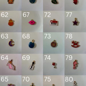 K&ouml;nnte beinhalten: Eine Sammlung von zwanzig kleinen Metallanh&auml;ngern, nummeriert von 61 bis 80, mit verschiedenen Emaille-Motiven wie einer Teekanne, Erdbeere, Lippen, Keyboard, Mond, Gitarre, K&uuml;rbis, Seepferdchen und einer Musiknote, jeweils mit einem Goldring.