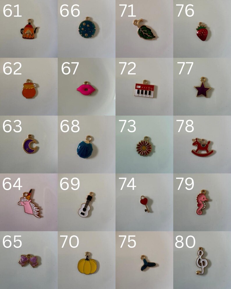 K&ouml;nnte beinhalten: Eine Sammlung von zwanzig kleinen Metallanh&auml;ngern, nummeriert von 61 bis 80, mit verschiedenen Emaille-Motiven wie einer Teekanne, Erdbeere, Lippen, Keyboard, Mond, Gitarre, K&uuml;rbis, Seepferdchen und einer Musiknote, jeweils mit einem Goldring.