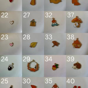 K&ouml;nnte beinhalten: Eine Sammlung von zwanzig kleinen Metallanh&auml;ngern, nummeriert von 21 bis 40, mit verschiedenen herbstlichen Motiven wie Herzen, Bl&auml;ttern, K&uuml;rbissen, H&auml;usern, Pilzen, einem Igel und einem Cupcake, jeweils mit einer kleinen &Ouml;se zur Befestigung.