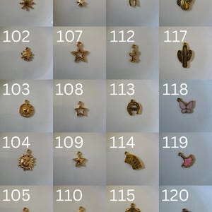 K&ouml;nnte beinhalten: Eine Sammlung von zwanzig kleinen goldfarbenen Metallanh&auml;ngern, nummeriert von 101 bis 120, mit verschiedenen Formen wie Sonnen, Sternen, Hufeisen, Kakteen, einem Schmetterling, einem F&auml;cher und einem Planeten, jeweils mit einer kleinen &Ouml;se.
