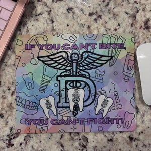 May include: A rectangular mouse pad with a pastel geometric background featuring dental icons and a central caduceus symbol over a large letter D. Three white teeth with USN anchor logos are displayed. Text reads: IF YOU CAN'T BITE, YOU CAN'T FIGHT!