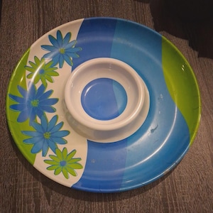 以下が含まれることがあります： 中央にディップボウルが付いた丸い仕切り付きサービング皿。プレートは、青、緑、白の配色と花の模様が特徴です。ディップボウルは白で、内側は青色です。スナックやディップの提供に最適です。