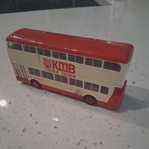 May include: A red and cream-colored double-decker bus toy with the text "KMB" and Chinese characters. The toy bus has multiple windows and red wheels. The roof of the bus is red.