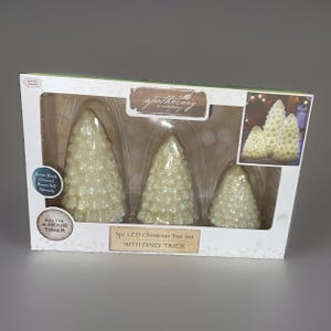 May include: A 3-piece LED Christmas tree set by Apothecary & Company in a white box. The set includes three cream-colored, textured, cone-shaped trees of varying heights. The packaging features text including 3pc LED Christmas Tree Set, With Daily Timer, and Built-in 4-Hour Timer.