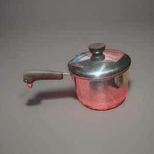 May include: A small stainless steel saucepan with a polished reflective finish, featuring a single gray handle extending from the side and a matching circular lid with a dark gray knob centered on top for easy lifting and secure coverage.