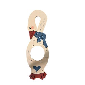 May include: A wooden goose-shaped kitchen utensil holder. The goose has a cream-colored body, a red beak, and a blue polka-dot scarf. The base features a blue heart and red feet. The holder has a circular opening.