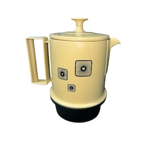 May include: A vintage cream-colored coffee pot with a black base and handle. The pot features three black geometric designs. The lid has a small handle. The spout is on the right side of the pot.