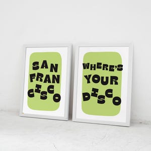 May include: Two framed art prints with white frames. One print reads "SAN FRANCISCO" in black, stylized text on a light green background. The other print says "WHERE'S YOUR DISCO" in black text on a light green background.