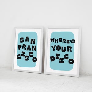 Puede incluir: Dos impresiones art&iacute;sticas enmarcadas. Una impresi&oacute;n dice "SAN FRANCISCO" en texto negro sobre un fondo azul claro. La otra impresi&oacute;n dice "WHERE'S YOUR DISCO" en texto negro sobre un fondo azul claro.
