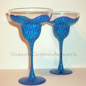 May include: Two blue and purple zebra print margarita glasses. The glasses are hand-painted with a blue and purple zebra print design.