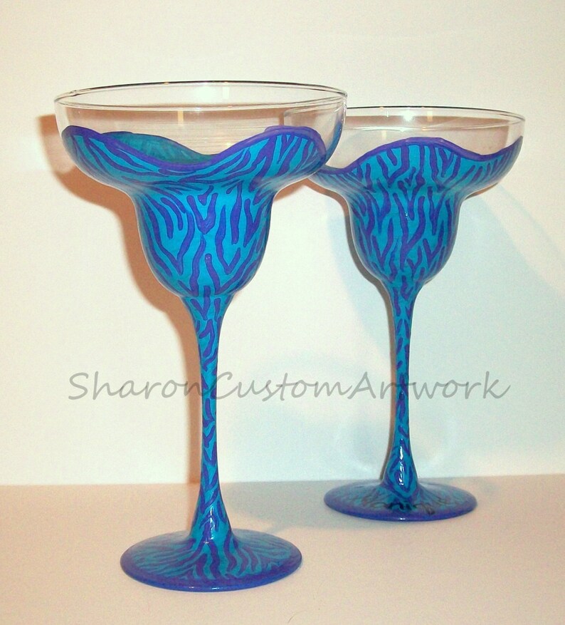 May include: Two blue and purple zebra print margarita glasses. The glasses are hand-painted with a blue and purple zebra print design.