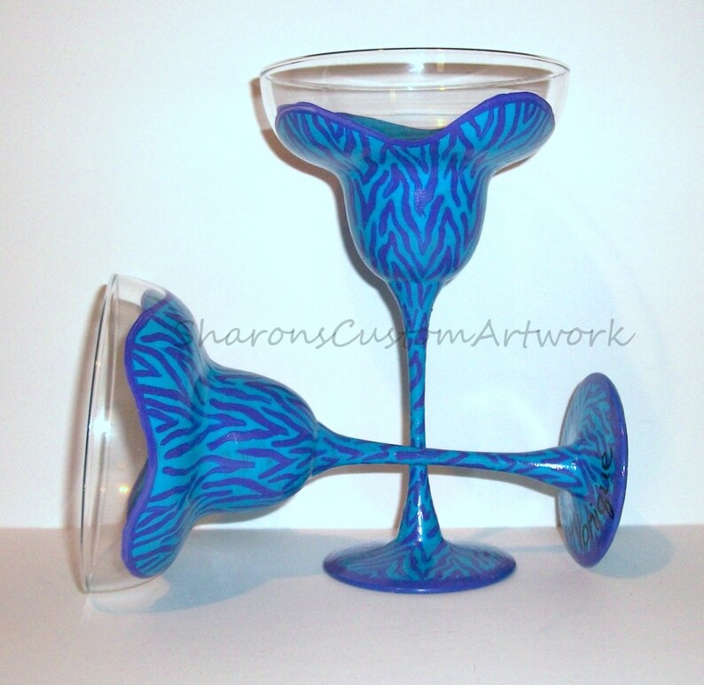 May include: Two blue and purple zebra print margarita glasses. The glasses are hand-painted with a blue and purple zebra print design.