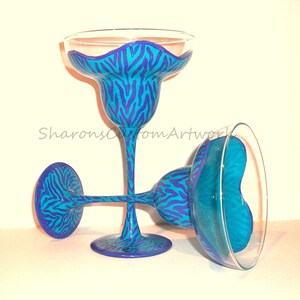 May include: Two turquoise and purple zebra print margarita glasses. The glasses are hand-painted with a blue and purple zebra print design.