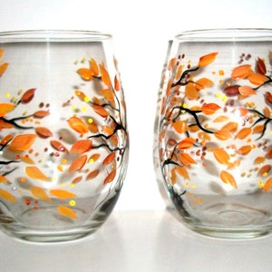 Op de afbeelding: Twee heldere glazen wijnglazen met handgeschilderde oranje en gele herfstbladeren en takken.