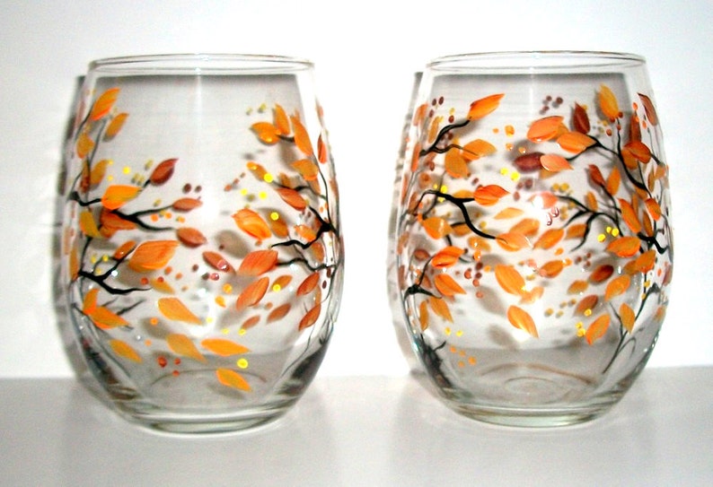 Op de afbeelding: Twee heldere glazen wijnglazen met handgeschilderde oranje en gele herfstbladeren en takken.