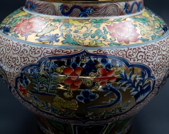 Könnte beinhalten: Eine dekorative Keramikvase mit einem breiten, abgerundeten Körper und einer schmalen Öffnung. Die Vase weist aufwendige Blumen- und Drachendesigns in Rot, Blau, Gold und Grün auf cremefarbenem Hintergrund auf. Der Rand ist mit Gold verziert.