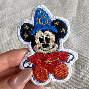 May include: Embroidered patch featuring a cartoon mouse in a wizard's outfit. The mouse wears a blue hat with gold stars and a crescent moon. The mouse's red robe has a gold star on the chest. The patch has a white border.