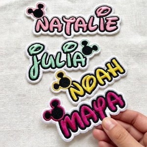 May include: Embroidered name patches in pink, green, and yellow with black accents. The names "Natalie", "Julia", "Noah", and "Maya" are displayed in a playful font, each with a Mickey Mouse head design.