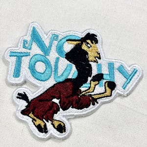 May include: Embroidered patch featuring a cartoon llama in shades of black, brown, and burgundy. The llama is set against a white background with the words "NO TOUCHY" in turquoise letters.
