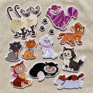 以下が含まれることがあります： 様々な漫画の猫が描かれた刺繍パッチのコレクション。シャム猫、チェシャ猫、その他の猫のキャラクターが様々なポーズと色で描かれています。小さな足跡のパッチも含まれています。