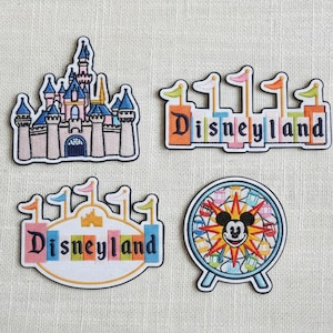 Könnte beinhalten: Vier gestickte Aufnäher mit Disneyland-Motiven. Ein Aufnäher zeigt ein Schloss mit blauen und rosa Akzenten. Die anderen zeigen das Wort "Disneyland" in bunten Buchstaben und ein Mickey Mouse-Riesenrad.