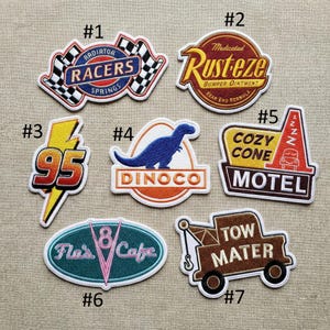 May include: Collection of seven embroidered patches featuring designs from the animated film "Cars." Designs include "Radiator Racers," "Rusteze," "95," a dinosaur, "Cozy Cone Motel," "Flo's Cafe," and "Tow Mater."