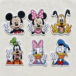 May include: A collection of six embroidered Disney character patches. Mickey and Minnie Mouse, Pluto, Goofy, Daisy Duck, and Donald Duck are depicted giving peace signs. Each patch has a white border and bright colours.