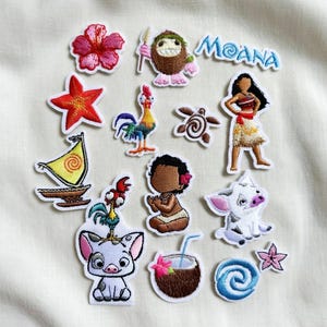 May include: A collection of embroidered patches featuring characters and elements from the animated film "Moana." Includes a pink hibiscus flower, a starfish, a rooster, a turtle, a sailboat, and the word "Moana."