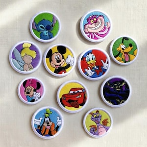 Può includere: Toppe ricamate raffiguranti vari personaggi Disney, tra cui Stitch, Stregatto, Trilli, Topolino, Paperino, Pluto, Minnie, Saetta McQueen, un cattivo e Figment. Ogni toppa è circolare con bordo bianco e colori vivaci.