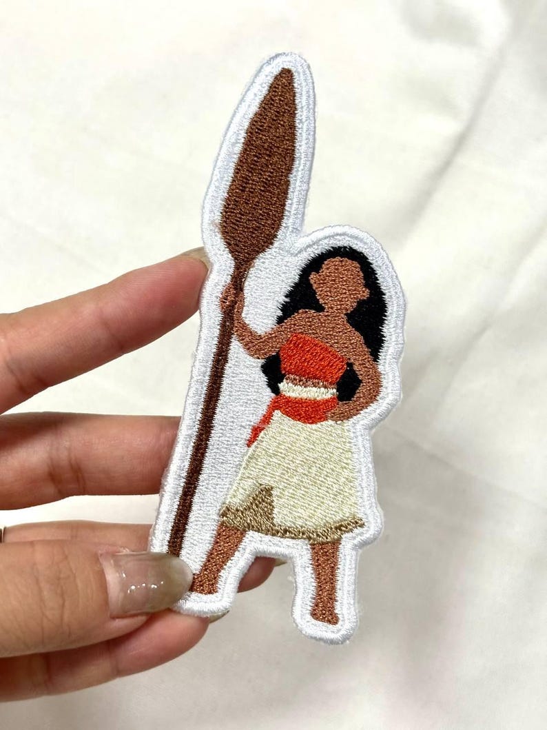 Op de afbeelding: Geborduurde patch met een Polynesische vrouw die een speer vasthoudt. De patch heeft een witte rand en toont de vrouw in een rode top, cr&egrave;mekleurige rok en bruine huid. De speer is bruin en de vrouw heeft zwart haar.
