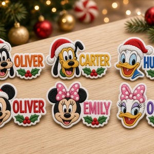 May include: Six embroidered patches featuring Disney characters wearing Santa hats, including Goofy, Pluto, Donald Duck, Mickey Mouse, Minnie Mouse, and Daisy Duck. Each patch includes a name: Oliver, Carter, Hudson, Oliver, Emily, and Olivia.