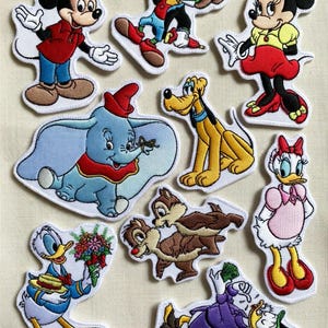 以下が含まれることがあります： ミッキーマウス、ミニーマウス、ドナルドダック、ダンボ、プルートなど、人気のディズニーキャラクターが刺繍されたパッチのコレクション。鮮やかな色使いで、白い縁取りが施されています。衣類やアクセサリーのデコレーションに最適です。