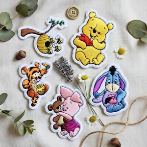 May include: Embroidered patches featuring Winnie the Pooh characters: Winnie the Pooh, Tigger, Eeyore, Piglet, and a beehive with bees. The patches are in various colors, including yellow, orange, pink, and blue, with white borders. A wooden button and sprigs of lavender and daisies are also present.