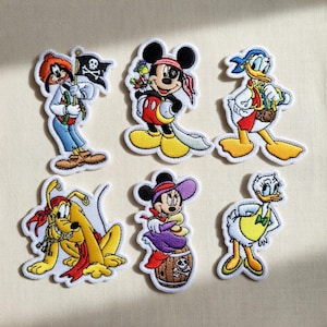 May include: Six embroidered patches featuring Disney characters in pirate attire. Characters include Goofy holding a pirate flag, Mickey Mouse with an eye patch, Donald Duck, Pluto, Minnie Mouse, and Daisy Duck. Each patch has a white border.