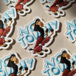 May include: Embroidered patches featuring a cartoon llama character in shades of black, brown, and red. The patches have a white border and the words "No Way" in light blue. The patches are scattered across a beige surface.