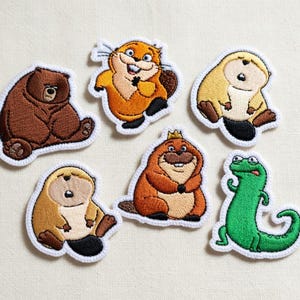 May include: Embroidered patches depicting cartoon animals: a brown bear, an orange beaver, a light brown beaver, a brown beaver with a crown, a green lizard, and a light brown beaver. Each patch has a white border and detailed stitching.