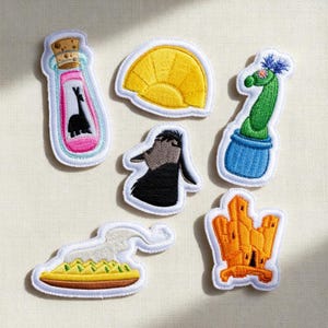 May include: A collection of embroidered patches featuring cartoon llamas, a cactus, a sun, and a cityscape. The patches are outlined in white with colorful details, including pink, yellow, blue, and orange. These patches are ideal for adding flair to clothing or accessories.