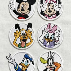 May include: Set of six embroidered patches featuring beloved Disney characters: Mickey Mouse, Minnie Mouse, Pluto, Daisy Duck, Donald Duck, and Goofy. Each character is in a circular white frame, making a peace sign or similar gesture.