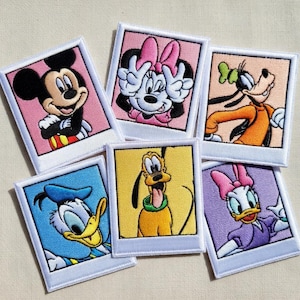 Peut inclure: Écussons brodés représentant des personnages Disney tels que Mickey Mouse, Minnie Mouse, Dingo, Donald Duck, Pluto et Daisy Duck. Chaque écusson présente un personnage dans un cadre coloré de style Polaroid avec une bordure blanche.