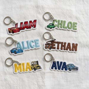 May include: Six embroidered keychains featuring names and cartoon car characters. The keychains display the names LIAM in red, CHLOE in green, ALICE in light blue, ETHAN in brown, MIA in yellow, and AVA in dark blue, each with a matching car.