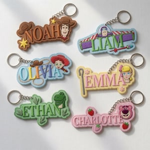 Op de afbeelding: Zes geborduurde vilt sleutelhangers met karakterthema's en namen: Noah met Woody, Liam met Buzz Lightyear, Olivia met Jessie, Emma met Bo Peep, Ethan met Rex en Charlotte met Lotso. Elke sleutelhanger is voorzien van een metalen ring.