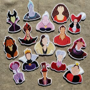 Può includere: Una collezione di toppe ricamate raffiguranti vari cattivi dei cartoni animati. Le toppe mostrano personaggi con caratteristiche distintive, tra cui Malefica, Ursula e la Regina di Cuori. Ogni toppa ha un bordo bianco e uno sfondo neutro.