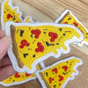 May include: Embroidered pizza slice patches with yellow cheese, red pepperoni, and a brown crust. The patches have a white border and are arranged on a wooden surface. These patches are ideal for adding to clothing or accessories.
