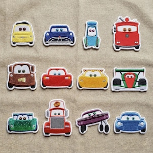 May include: A selection of embroidered car patches in various colours, including yellow, blue, red, and green. The patches feature different car designs, such as a race car, a tow truck, and a classic car. Each patch has a white border.