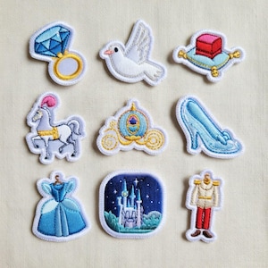 May include: A collection of nine embroidered patches featuring fairytale-themed designs. The patches include a blue gemstone ring, a white dove, a red box on a blue pillow, a white horse, a golden carriage, a blue glass slipper, a blue dress, a castle, and a prince's outfit.