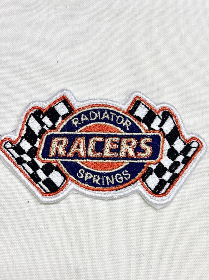 May include: Embroidered patch featuring the text "Radiator Racers Springs" in a circular design with a blue and orange color scheme. Two checkered flags flank the design, all outlined in white.