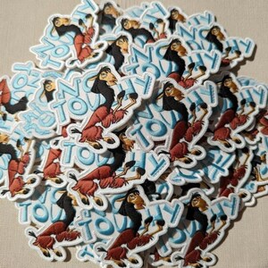 May include: A pile of embroidered patches featuring a cartoon llama character with a black mane and red fur. The patches have a white border and the words "NO TOUCHY" in blue letters.