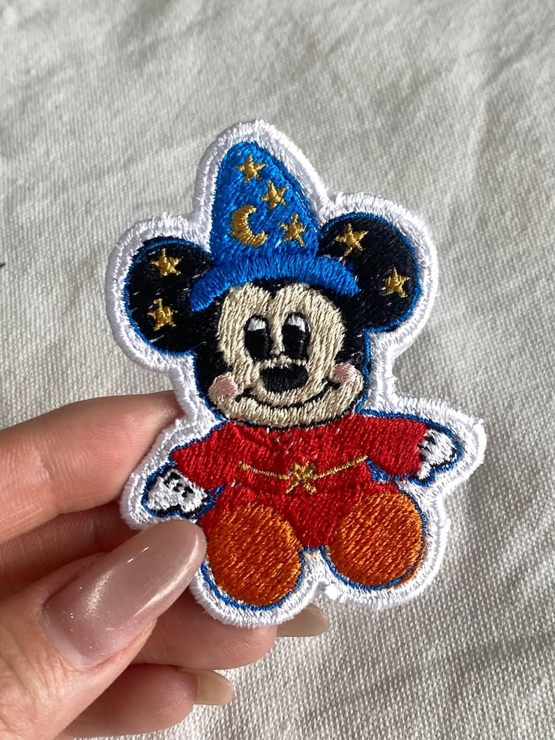 May include: Embroidered patch featuring a cartoon mouse in a wizard's outfit. The mouse wears a blue hat with gold stars and a crescent moon. The mouse's red robe has a gold star on the chest. The patch has a white border.