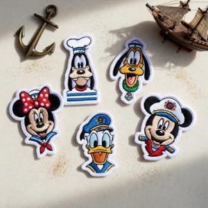 May include: Embroidered patches featuring cartoon characters in sailor outfits. The patches include Mickey Mouse, Minnie Mouse, Donald Duck, Goofy, and Pluto. A bronze anchor and a miniature sailboat are also present.